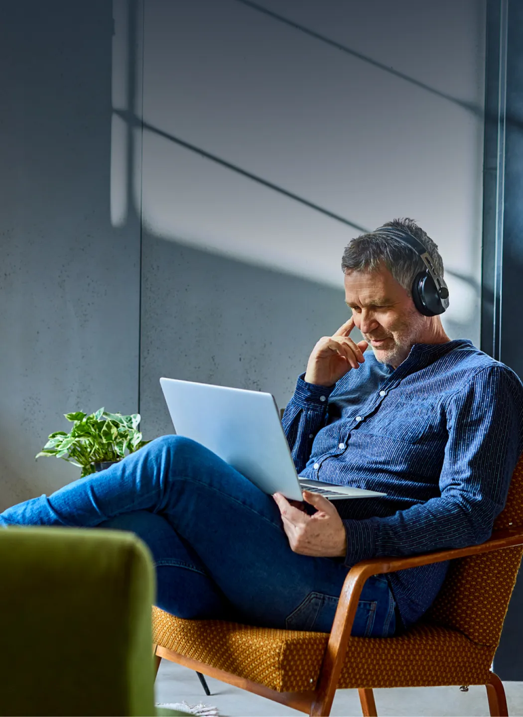 Man with headphones on relaxing in a chair and browsing his laptop